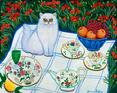 This white persian cat is sitting on a quilt outside with pretty china and a bowl of fruit .