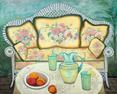 A whitr ratan couch with a soft butter yellow rose print textile on the cushions with a table in front with a pitcher of lemonaide and a bowl of peaches.